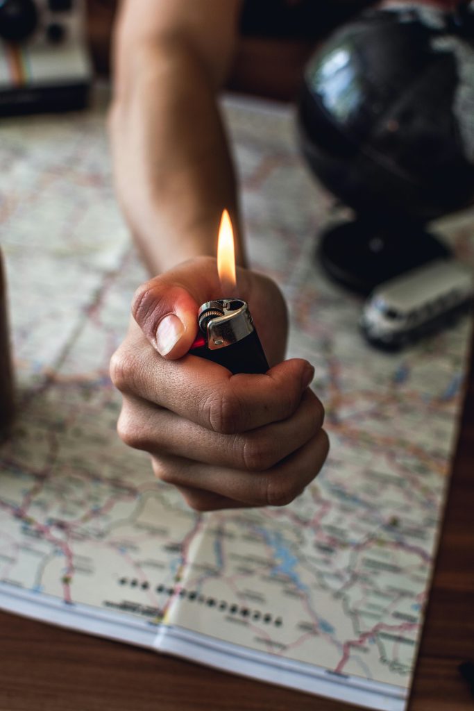 Close-up of a hand holding a lighter over a travel map, planning an adventure.